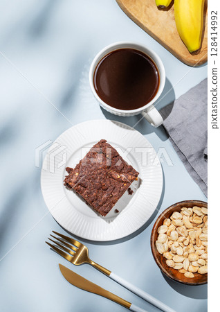 Chocolate banana brownie on a plate on a blue background with a cup of coffee, nuts Chocolate banana brownie on a plate on a blue background with a cup of coffee, nuts 128414992