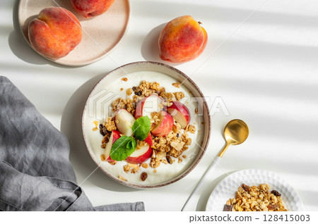 Natural greek yogurt with granola or muesli, peach and mint in a bowl on a white background 128415003