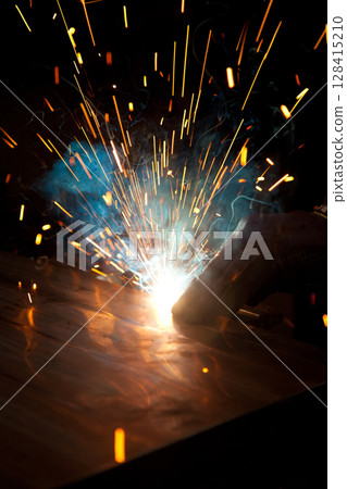 Welder uses torch to make sparks during manufacture of metal equipment, industrial professional worker 128415210