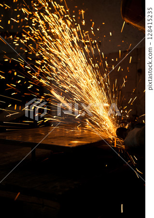 Worker working in industry or factory is holding a cutting stone or grinding stone and sparks are coming out of the metal Worker working in industry or factory is holding a cutting stone or grinding stone and sparks are coming out of the metal 128415235