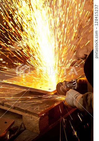 Worker working in industry or factory is holding a cutting stone or grinding stone and sparks are coming out of the metal Worker working in industry or factory is holding a cutting stone or grinding stone and sparks are coming out of the metal 128415237