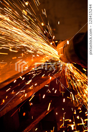 Worker working in industry or factory is holding a cutting stone or grinding stone and sparks are coming out of the metal 128415244