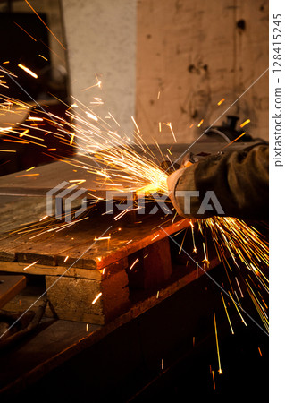 Worker working in industry or factory is holding a cutting stone or grinding stone and sparks are coming out of the metal Worker working in industry or factory is holding a cutting stone or grinding stone and sparks are coming out of the metal 128415245
