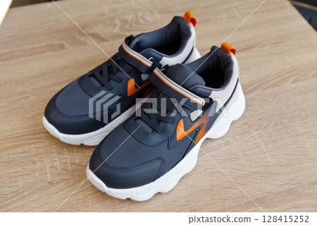Stylish comfortable and useful grey or blue orange sneakers, on oak wooden floor 128415252