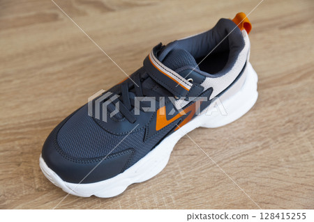 Stylish comfortable and useful grey or blue orange sneakers, on oak wooden floor 128415255