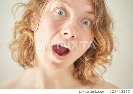 Caucasian female with curly hair showing surprised expression close-up portrait 128415377