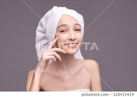Young caucasian female skincare routine smiling with towel and cream on face 128415429