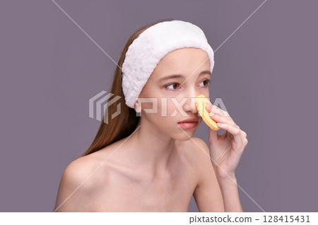 Young caucasian female skincare routine with facial sponge and white headband Young caucasian female skincare routine with facial sponge and white headband 128415431