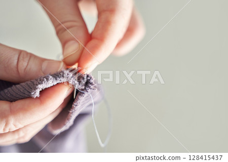 Close-up of adult hands sewing fabric with needle and thread for handcrafted Close-up of adult hands sewing fabric with needle and thread for handcrafted 128415437