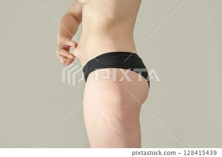 Young caucasian female pinching skin on waist in black underwear showing body 128415439