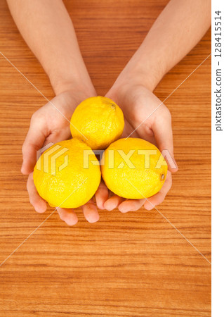 Young Caucasian male holding yellow lemon in hand over brown wooden table Young Caucasian male holding yellow lemon in hand over brown wooden table 128415514