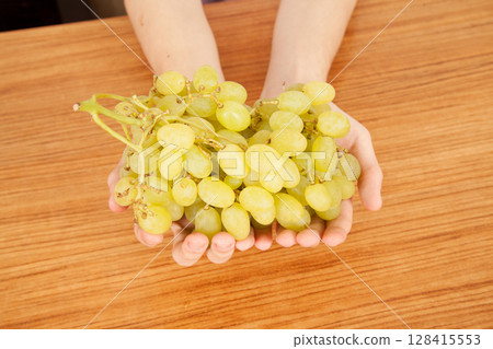 Caucasian man holding bunch of yellow ripe grapes on a wooden table 128415553