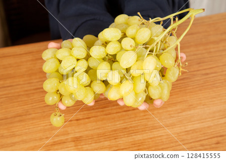 Caucasian man holding bunch of yellow ripe grapes on a wooden table Caucasian man holding bunch of yellow ripe grapes on a wooden table 128415555
