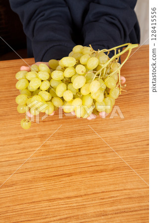 Caucasian man holding bunch of yellow ripe grapes on a wooden table Caucasian man holding bunch of yellow ripe grapes on a wooden table 128415556