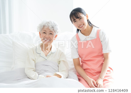 A female caregiver caring for a senior woman lying in bed 128416409