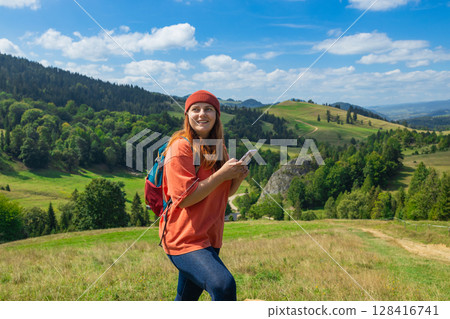 Smiling female hiker navigating with smartphone in scenic mountain landscape 128416741