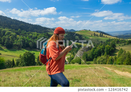 Smiling female hiker navigating with smartphone in scenic mountain landscape 128416742
