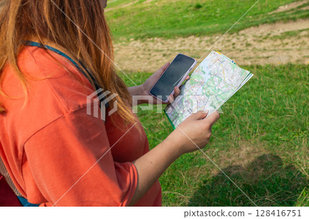 Young Female Hiker Navigating Trail with Map and Smartphone 128416751