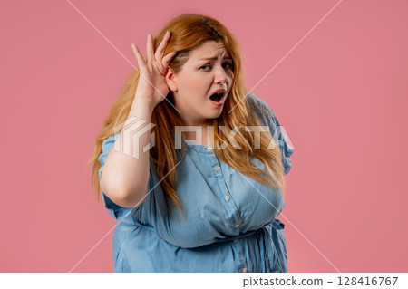Plus size woman pointing ear with confused face, signaling she cant hear clearly 128416767