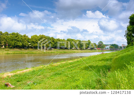embankment of a river uzh in summer. longest linden alley in europe on a sunny day. view of lush trees near water under blue sky with clouds. beautiful urban landscape of ukraine for travel 128417138