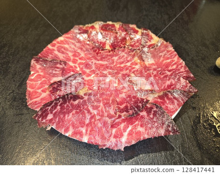 Thinly sliced cecina on dark stone background. Cecina - the famous Spanish salted and dried meat. Made from Angus beef. Top view. Flat lay 128417441