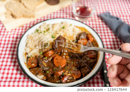 Fork holding piece of meat over bowl of beef stew with rice Fork holding piece of meat over bowl of beef stew with rice 128417644