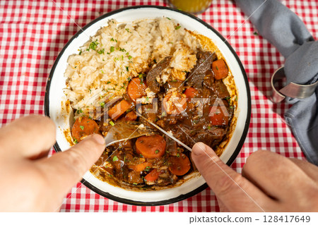 Hands cutting into hearty beef stew with rice Hands cutting into hearty beef stew with rice 128417649