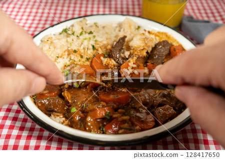 Hands cutting into hearty beef stew with rice Hands cutting into hearty beef stew with rice 128417650