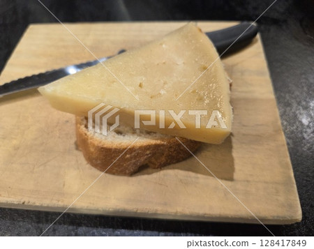 Gourmet cheese slice on bread with knife on wooden board. World Cheese Day. Spanish tapas 128417849