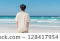 A male student in a T-shirt standing on a white sandy beach with an emerald green sea | Refreshing 128417954