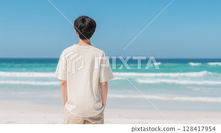 A male student in a T-shirt standing on a white sandy beach with an emerald green sea | Refreshing 128417954