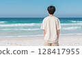 A male student in a T-shirt standing on a white sandy beach with an emerald green sea | Refreshing 128417955