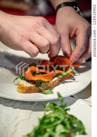 Chef hands preparing salmon sandwich with arugula 128418402