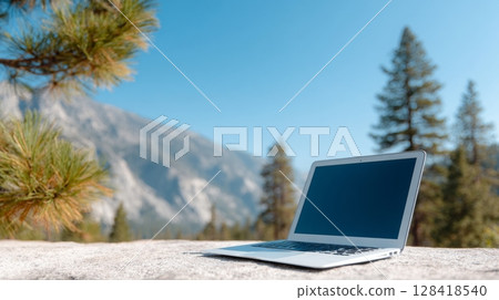 Laptop placed on a rock surface in a serene outdoor setting, surrounded by tall trees and mountains, ideal for a workcation experience 128418540