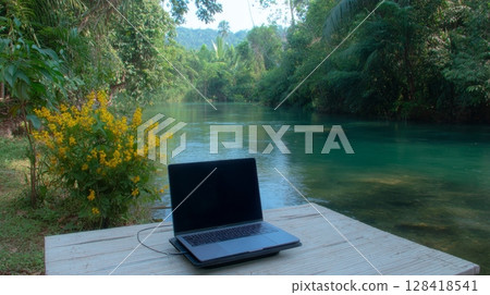 Laptop on wooden table by serene river surrounded by lush greenery, illustrating the concept of digital nomad workcation lifestyle Laptop on wooden table by serene river surrounded by lush greenery, illustrating the concept of digital nomad workcation lifestyle 128418541