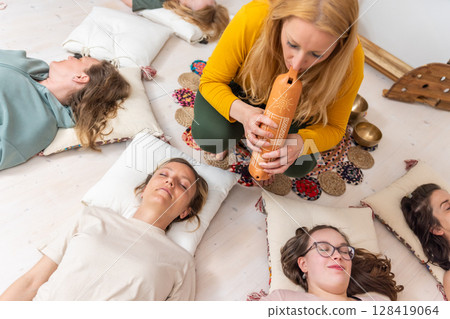 Group therapy session with Tibetan singing bowls for group of women lying on wooden floor surrounded by copper bowls. Meditation and relaxation 128419064
