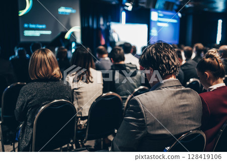 Speaker giving a talk in conference hall at business event. Rear view of unrecognizable people in audience at the conference hall. Business and entrepreneurship concept 128419106