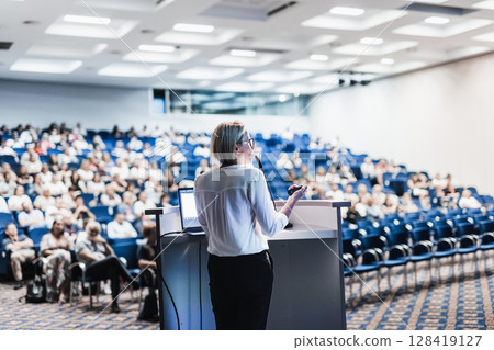 Female speaker giving a talk on corporate business conference. Unrecognizable people in audience at conference hall. Business and Entrepreneurship event Female speaker giving a talk on corporate business conference. Unrecognizable people in audience at conference hall. Business and Entrepreneurship event 128419127