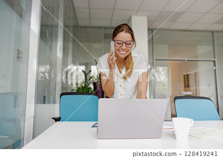 A Professional Woman is Working Remotely while using her Laptop and Phone for Tasks A Professional Woman is Working Remotely while using her Laptop and Phone for Tasks 128419241