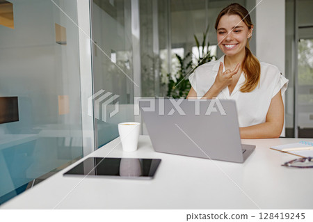 A Smiling Woman Working Enthusiastically on Her Laptop in a Modern Office Environment 128419245