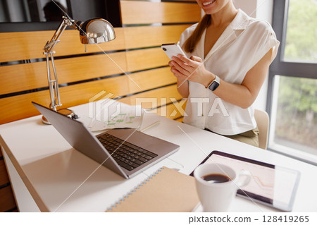 A skilled woman works with a laptop and smartphone in a modern, creative workspace 128419265