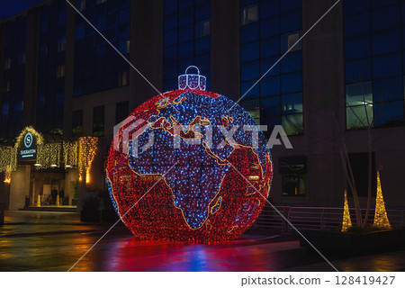 A glowing globe shaped decoration with red and blue continents stands near a Sheraton hotel in Brussels, surrounded by golden lights and holiday decor at night. 128419427