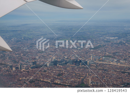 Aerial perspective of Brussels featuring skyscrapers, low rise buildings, a central park, and surrounding countryside, with a plane wing visible. 128419543