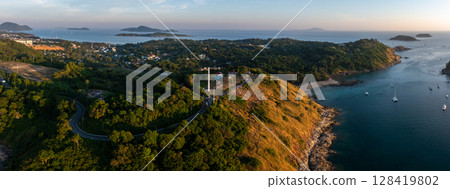 Aerial view of Naiharn Beach in Phuket, Thailand, featuring a hilltop wind turbine, anchored boats, lush greenery, and islands across a calm sea. Aerial view of Naiharn Beach in Phuket, Thailand, featuring a hilltop wind turbine, anchored boats, lush greenery, and islands across a calm sea. 128419802