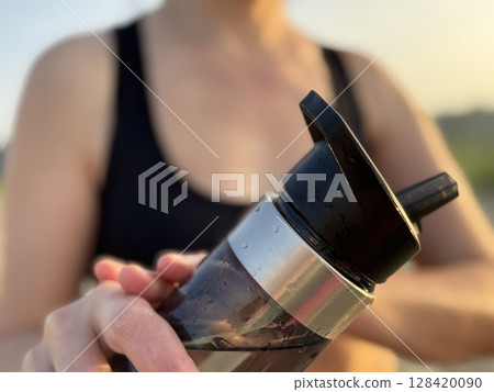 Close up of athletic woman hand holding shaker bottle with water on sandy trail near forest, outdoor fitness and healthy lifestyle concept Close up of athletic woman hand holding shaker bottle with water on sandy trail near forest, outdoor fitness and healthy lifestyle concept 128420090