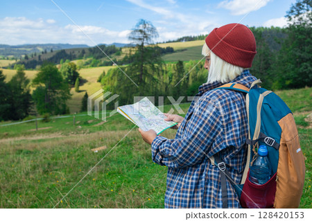 Young Woman Hiking with Map and Smartphone in Scenic Countryside Young Woman Hiking with Map and Smartphone in Scenic Countryside 128420153