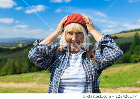 Happy senior woman enjoying a scenic mountain hike on a sunny day 128420177