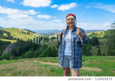 Smiling senior woman giving thumbs up while hiking in the mountains Smiling senior woman giving thumbs up while hiking in the mountains 128420253