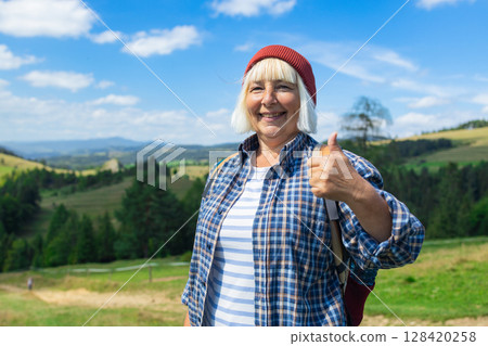 Smiling senior woman giving thumbs up while hiking in the mountains 128420258