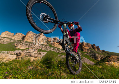 Young man riding through the air on a mountain bike on the back wheel. Fitness, extreme sports and mountain bike with man outdoors for cycling, jumping and adventure. Adrenaline junkie 128421245